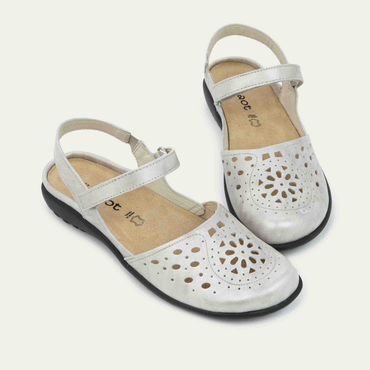 Pair of silver flat shoes with a perforated design, open heel, and adjustable ankle strap on a black sole