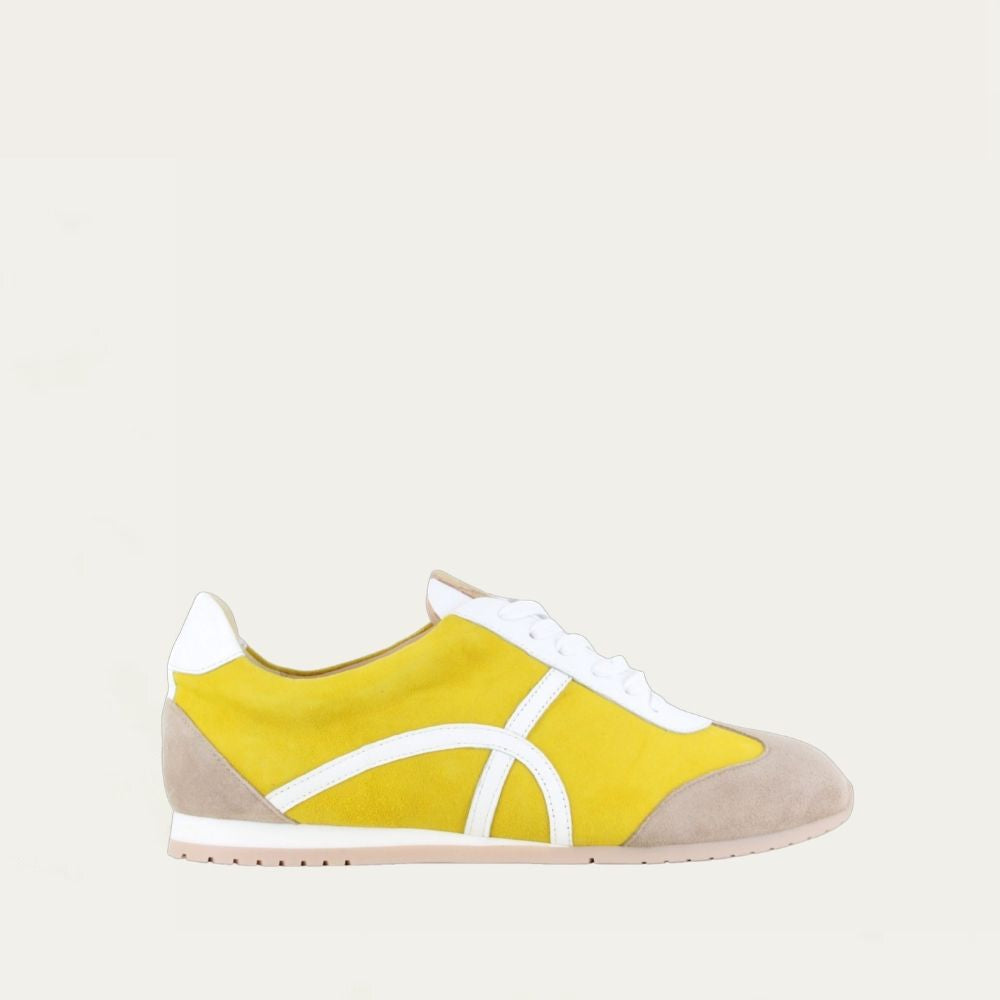 Profile view of a yellow suede sneaker with a swirl accent on the side on a low white and beige sole.
