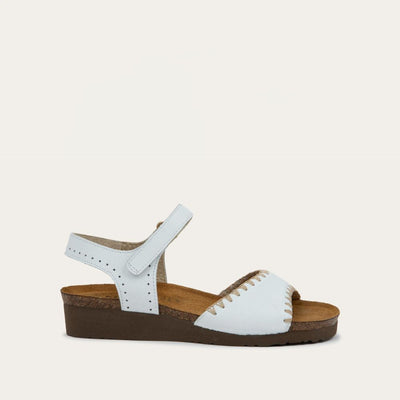 Profile view of a white sandal featuring a toe strap with contrast stitiching, adjustable ankle strap, and a cork footbed.