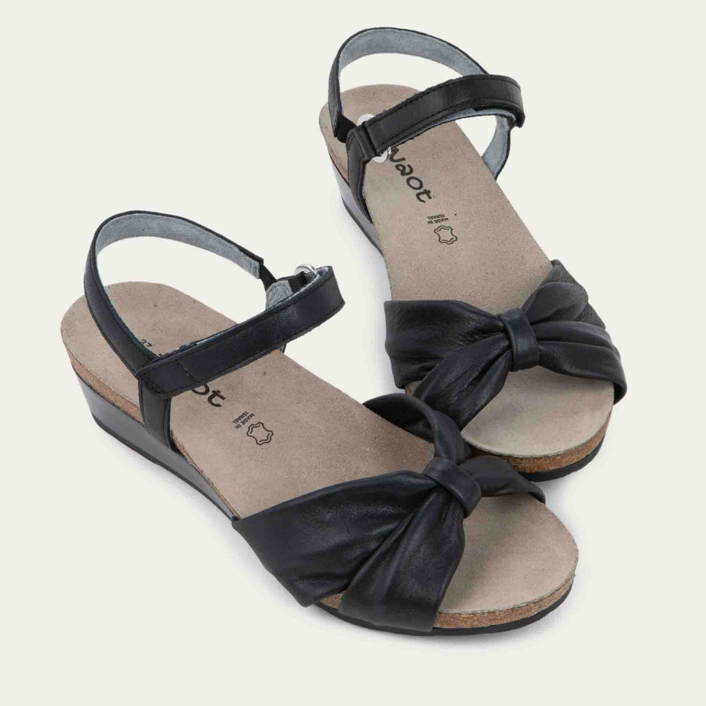 A pair of black wedge sandals with an ankle strap and twisted front strap, featuring a cork footbed and wedge heel.