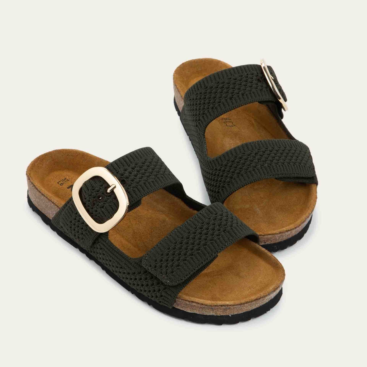 Pair of blue slip-on sandals with two adjustable knit straps and a large gold buckle. It has a cork footbed and a black sole.