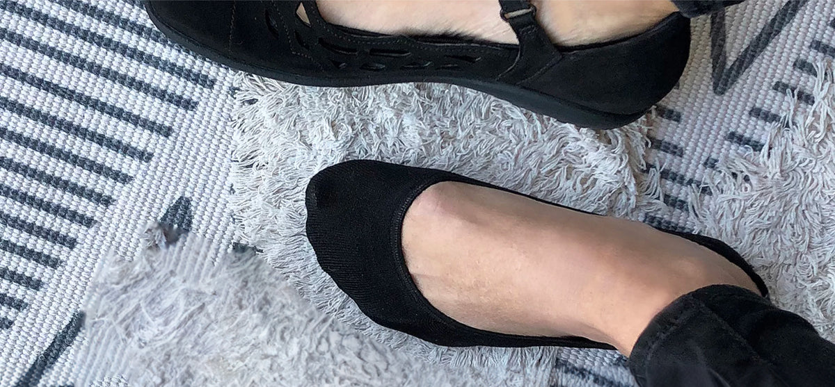 Close-up of a person wearing black ballet flats, standing on a textured rug.