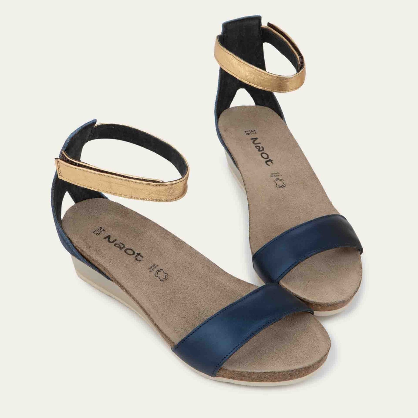Pair of blue wedge sandals with cork sole, featuring an open toe and metallic gold ankle strap.