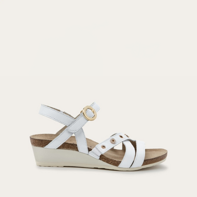 A white sandal with faux buckle hook and loop closure and eye-catching hardware ornamentation on a white background.