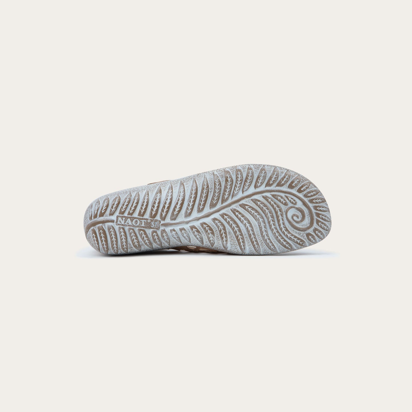 Bottom view of a Tan suede Mary Jane shoe with cut-out patterns, a Velcro strap, and a textured gray sole, set against a plain white background. Casual and stylish.
