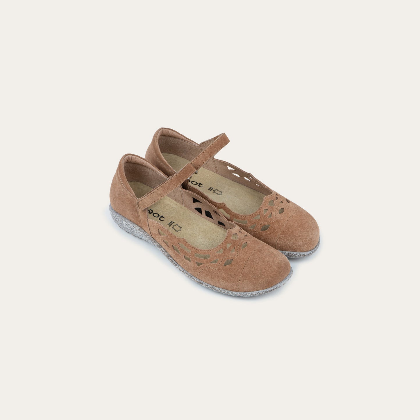 Pair of Tan suede Mary Jane shoes with cut-out patterns, Velcro straps, and textured gray soles, set against a plain white background. Casual and stylish.