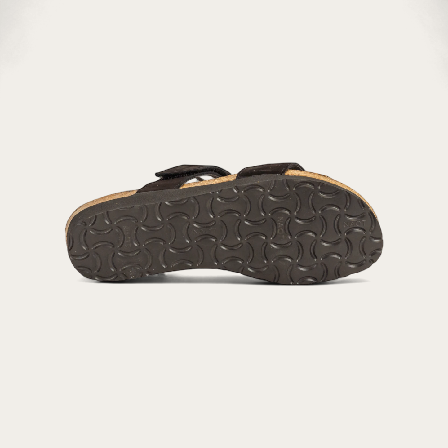 Bottom view of a black leather slip on wedge sandal with two straps and reivet detailing on a cork footbed,