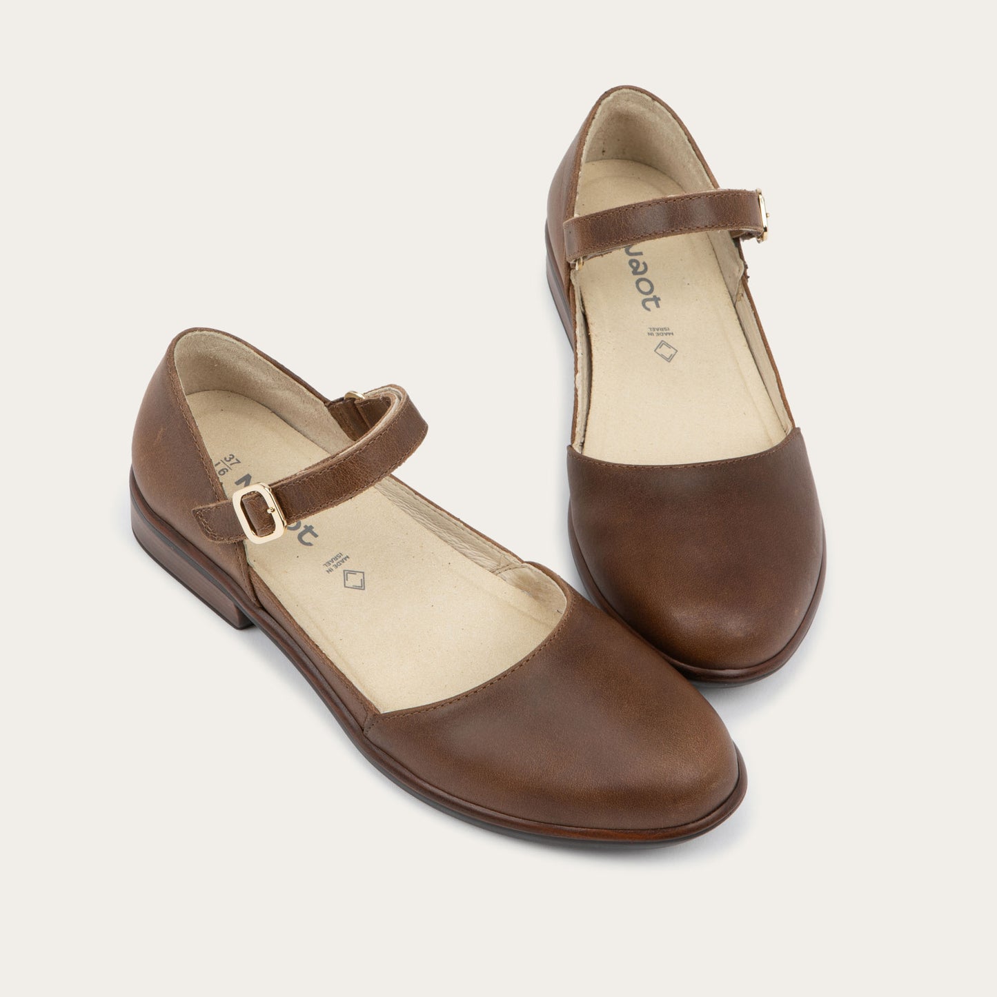 A pair of of a brown maryjanes with a simple buckle strap on a black and brown sole