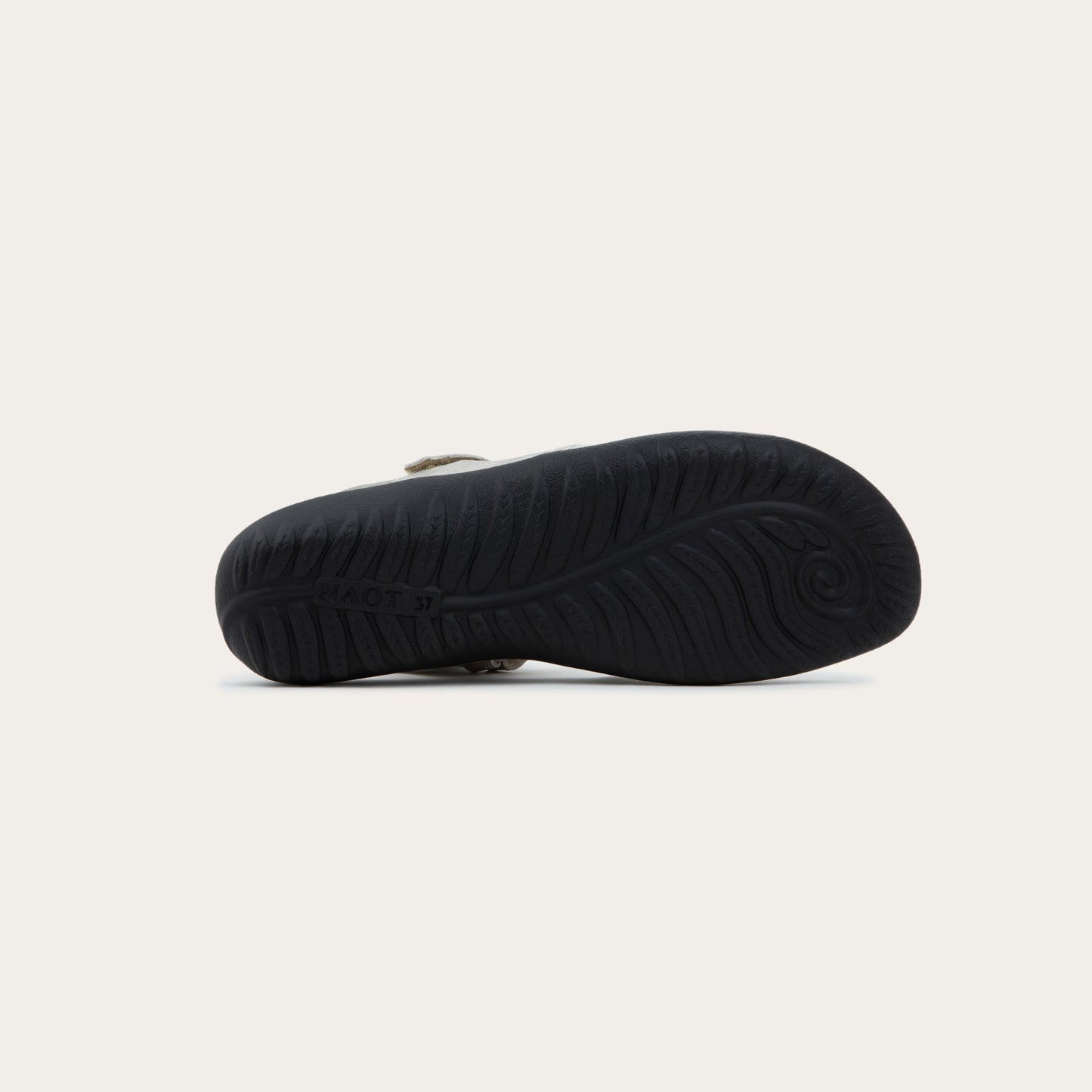 Bottom view of a silver flat shoe with a perforated design, open heel, and adjustable ankle strap on a black sole