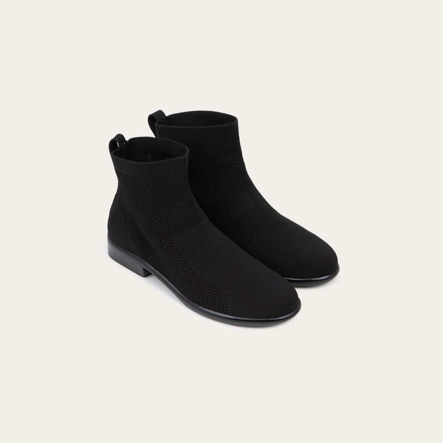 A pair of of black ankle boots featuring a textured knit uppers, pull tabs at the heels, and low, flat black soles.