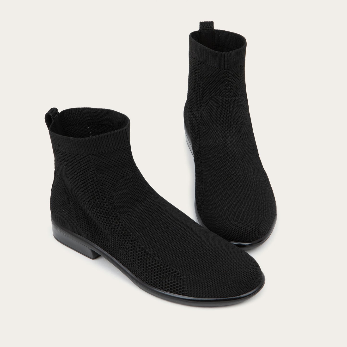 A pair of of black ankle boots featuring a textured knit uppers, pull tabs at the heels, and low, flat black soles.