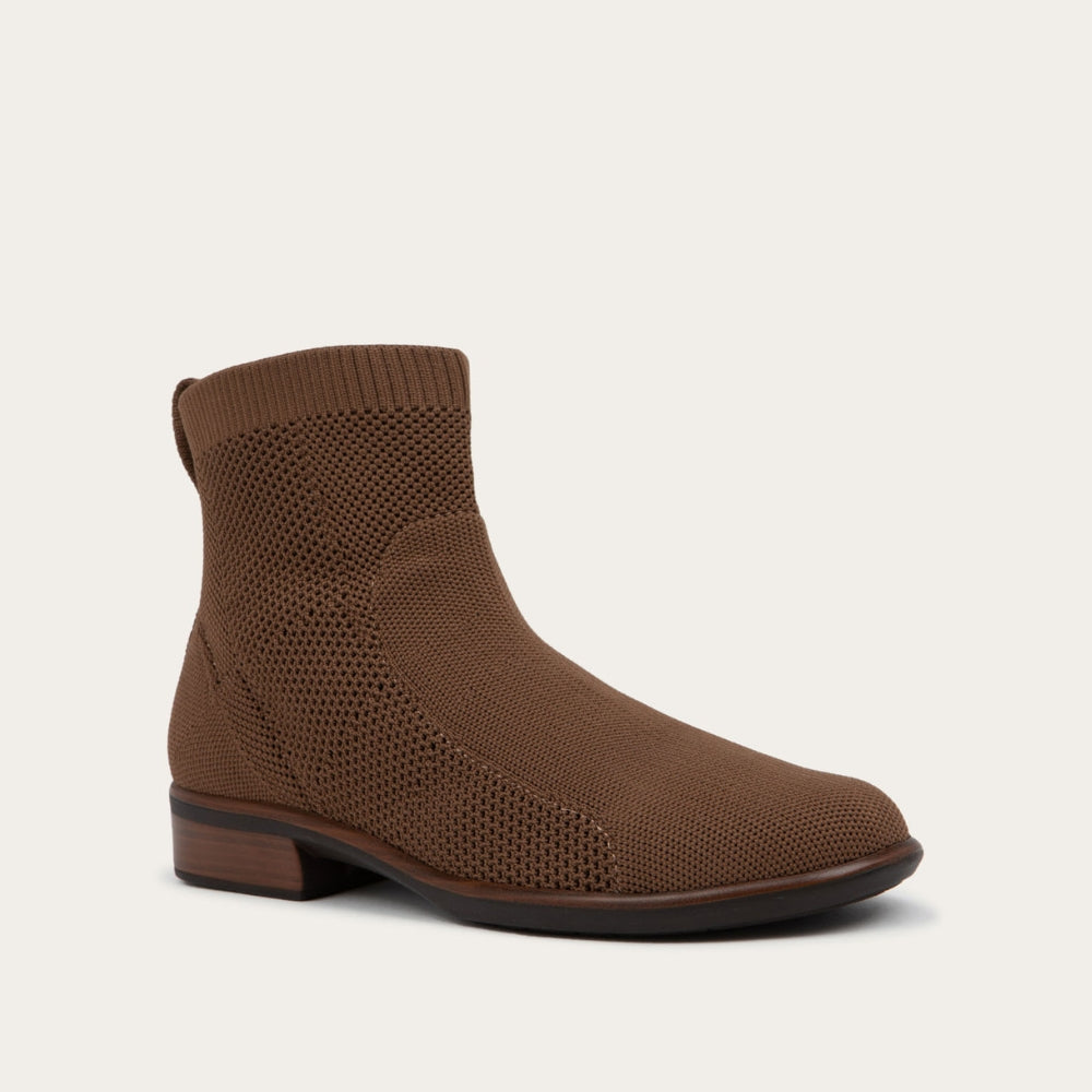 Angled profile view of a brown ankle boot featuring a textured knit upper, a pull tab at the heel, and a low, flat brown sole.