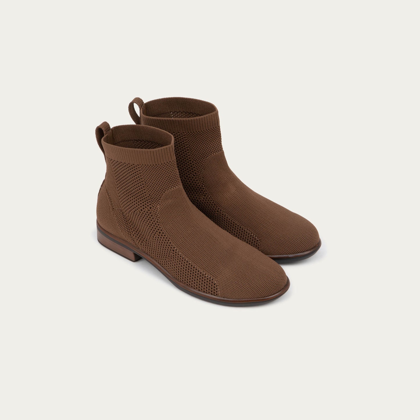 A pair of of brown ankle boots featuring a textured knit uppers, pull tabs at the heels, and low, flat brown soles.