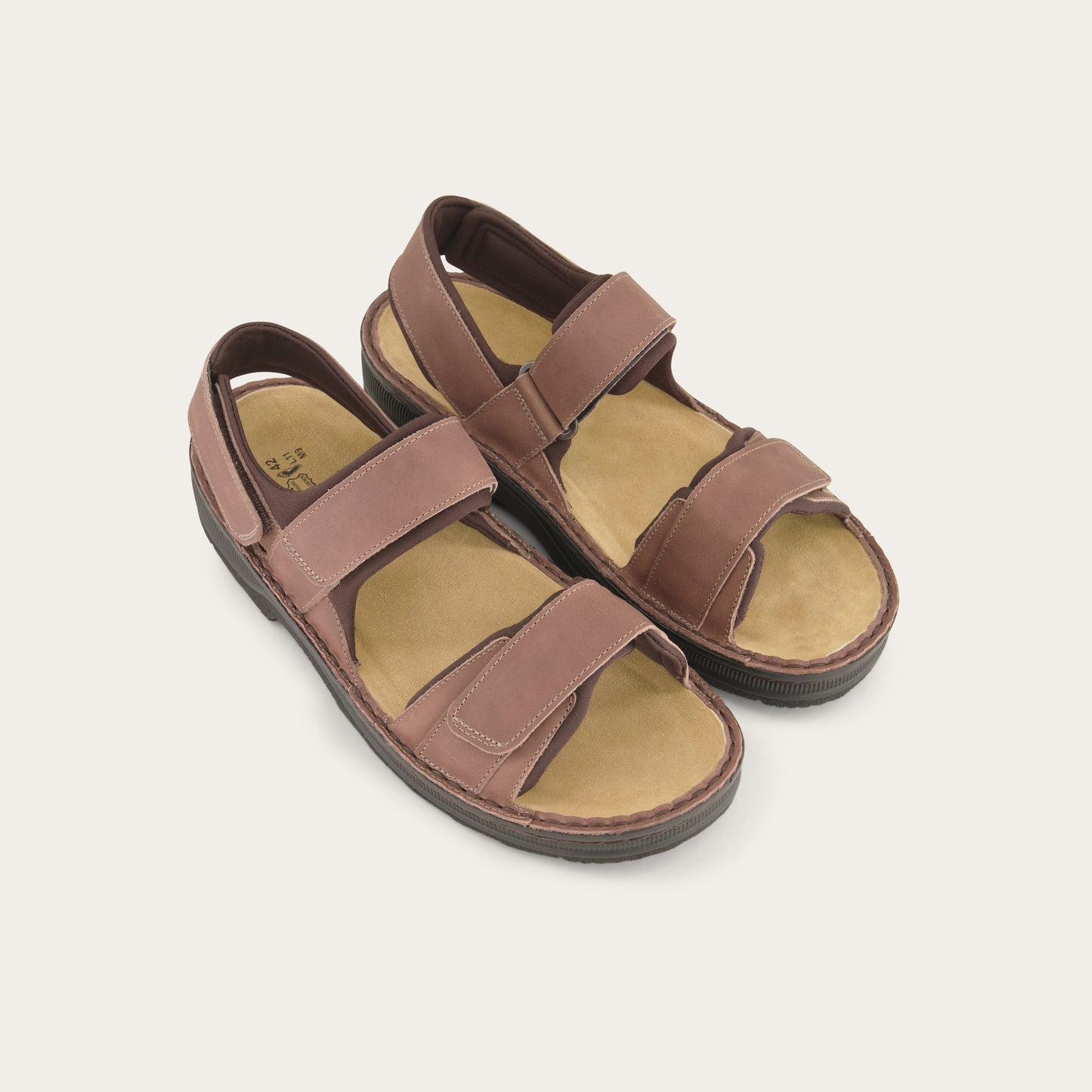 Pair of  brown nubuck sandals featuring 3 hook and loop straps around the foot and ankle for adjustability on a black sole.