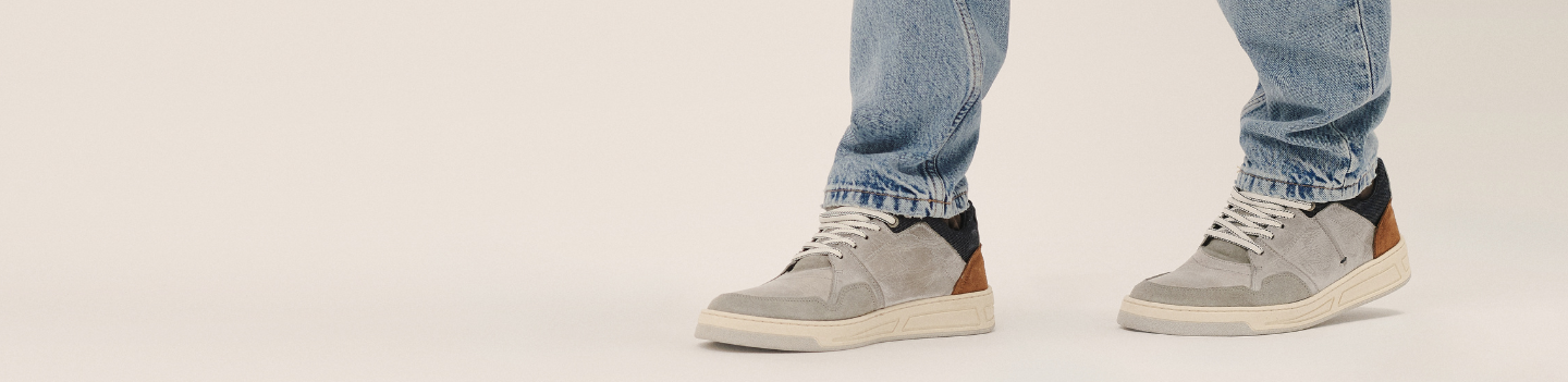 Gray sneakers with black accents worn with light blue jeans on a white background