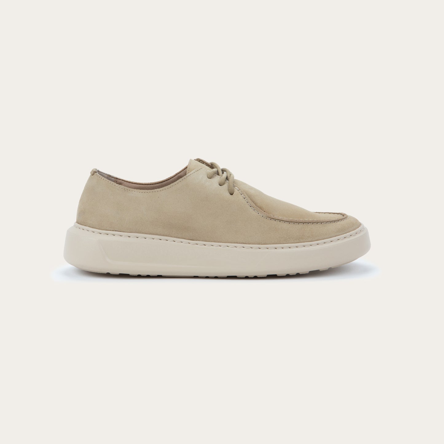 Profile view of a  beige suede lace-up sneaker with a thick, matching rubber sole and a  stitched toe.