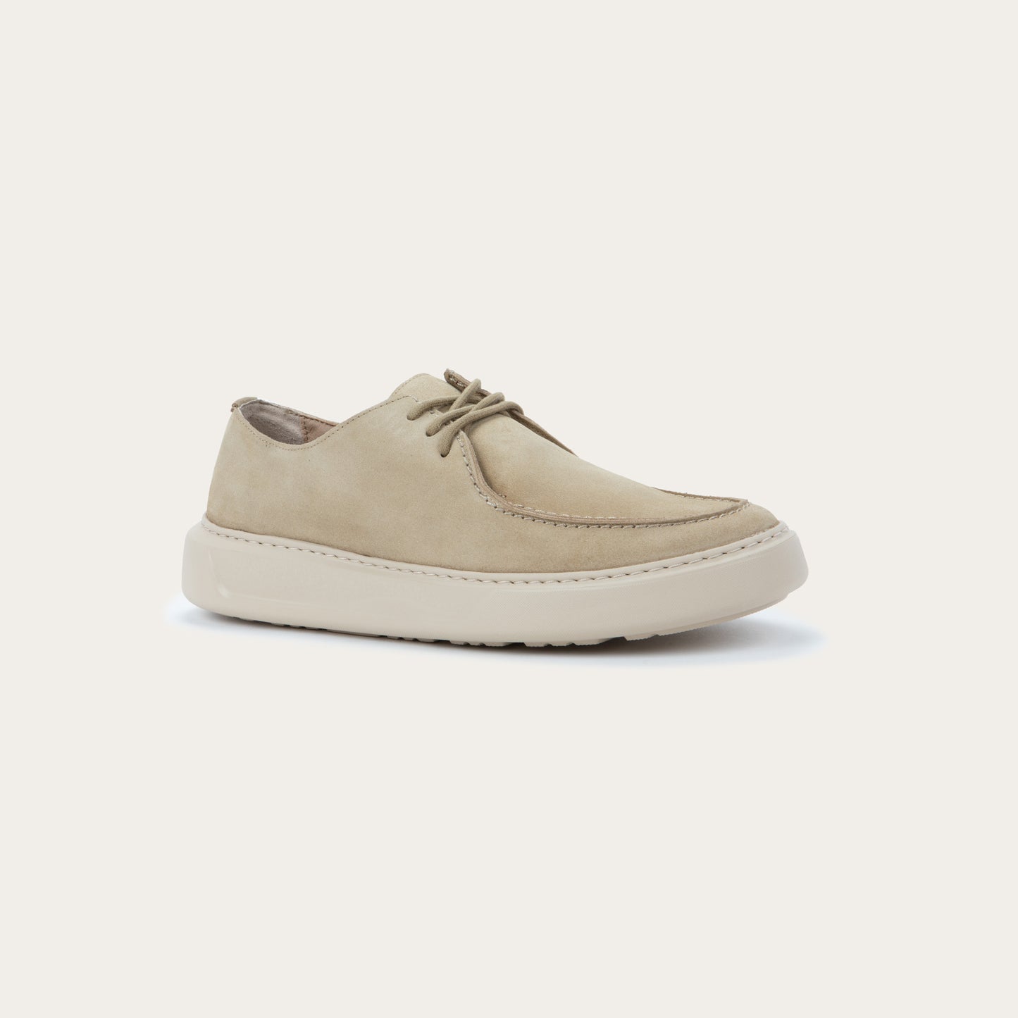 Angled profile view of a beige suede lace-up sneaker with a thick, matching rubber sole and a  stitched toe.