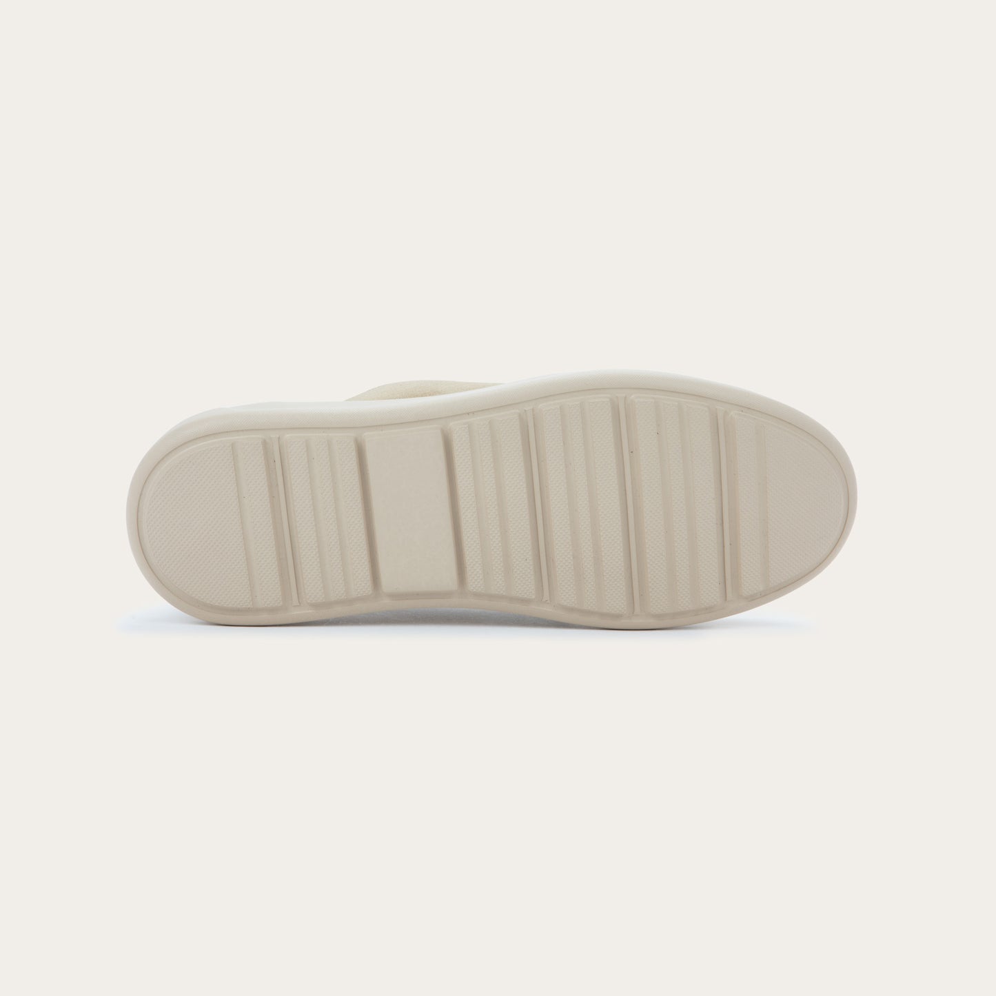 Bottom view of a beige suede lace-up sneaker with a thick, matching rubber sole and a  stitched toe.