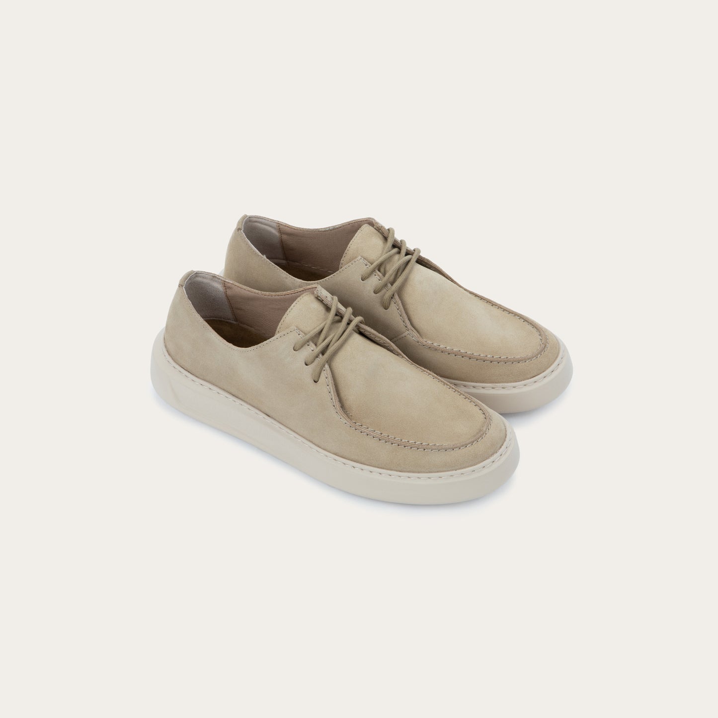 Pair of beige suede lace-up sneakers with a thick, matching rubber soles and  stitched toes.