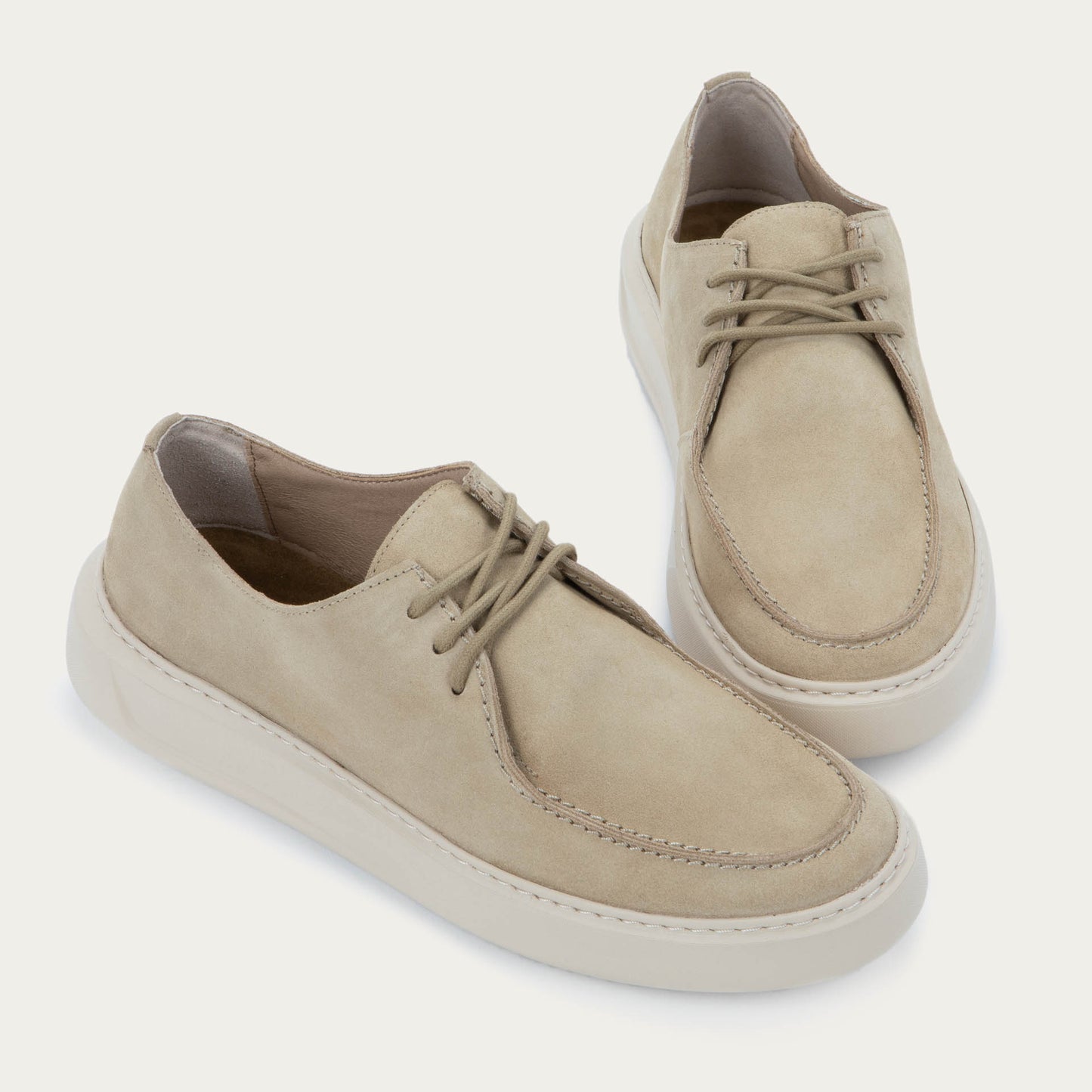 Pair of beige suede lace-up sneakers with a thick, matching rubber soles and  stitched toes.