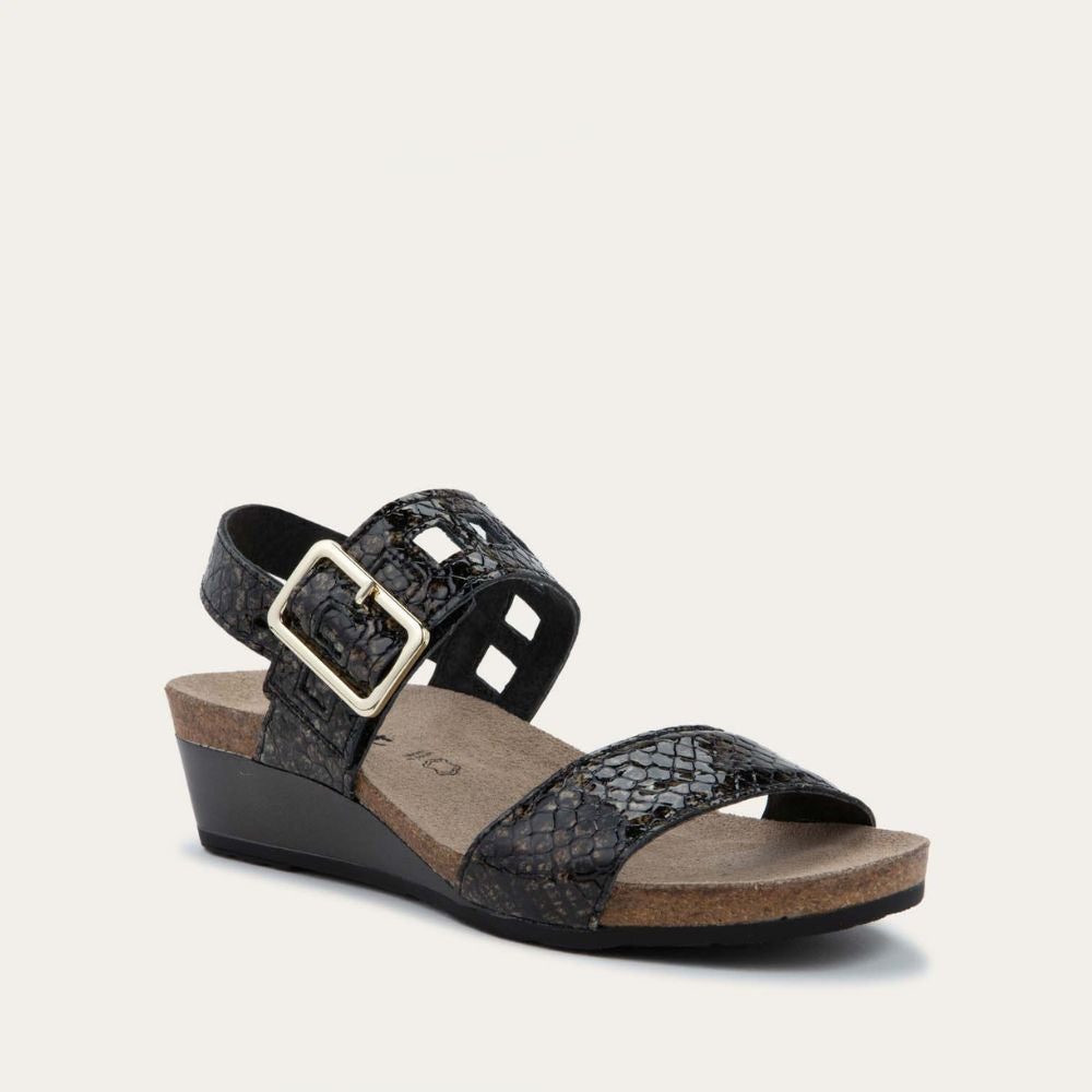 Angled profile view of a black wedge sandal with a faux snakeskin texture, featuring two straps and metallic buckles. The cork footbed adds a natural touch.