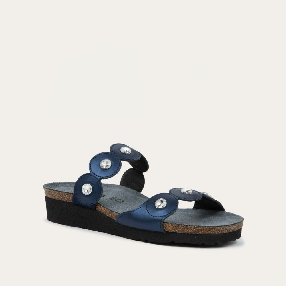 Angled profile view of navy blue sandal with cork wedge sole. Features two straps with circular details and large round silver studs.