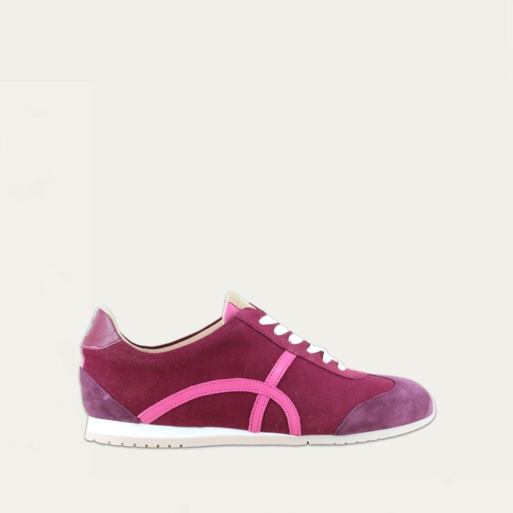 Profile view of a purple suede sneaker with a swirl accent on the side on a low white and beige sole. 