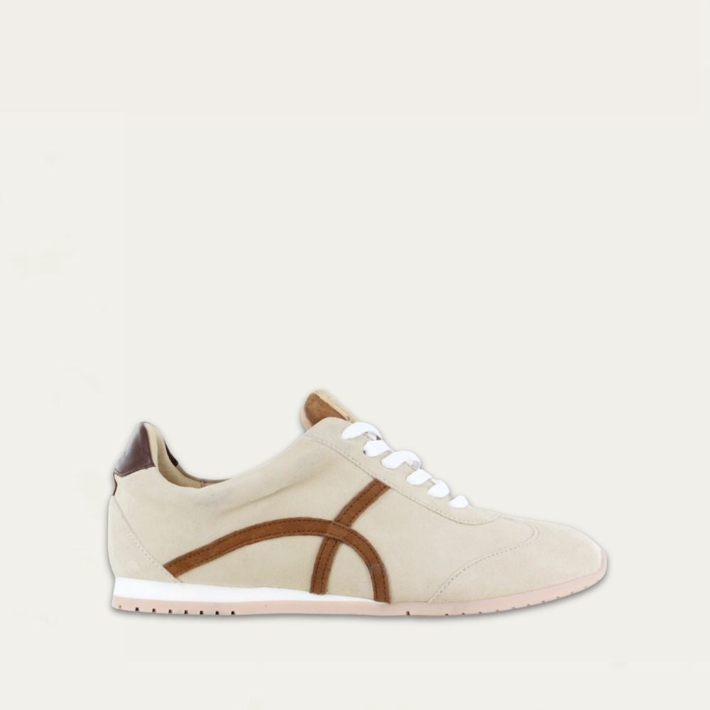 Profile view of a beige suede sneaker with a swirl accent on the side on a low white and beige sole. 