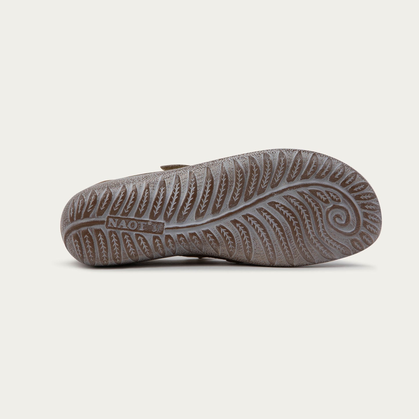 Bottom view of a brown Mary Jane flat with metallic strap, suede upper, and textured sole.