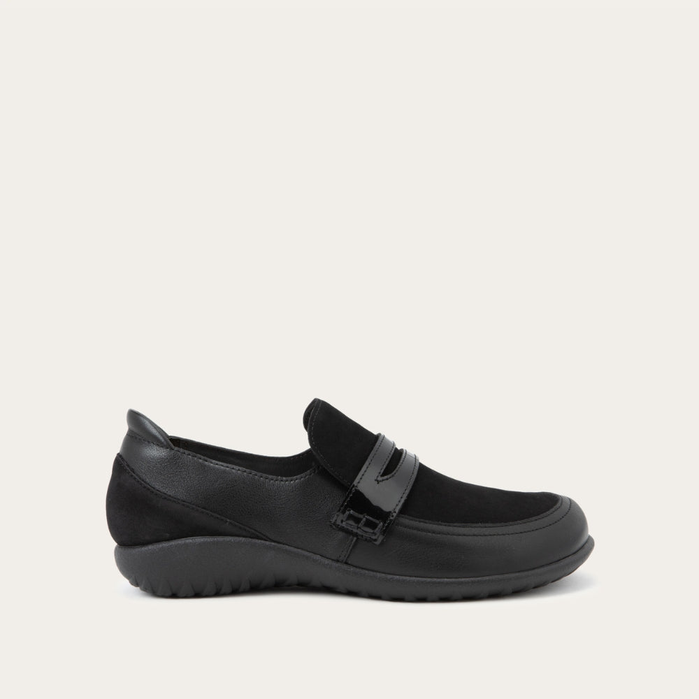 Side view of a black slip-on loafer featuring a mix of matte leather and soft suede textures with a glossy patent leather strap across the vamp.
