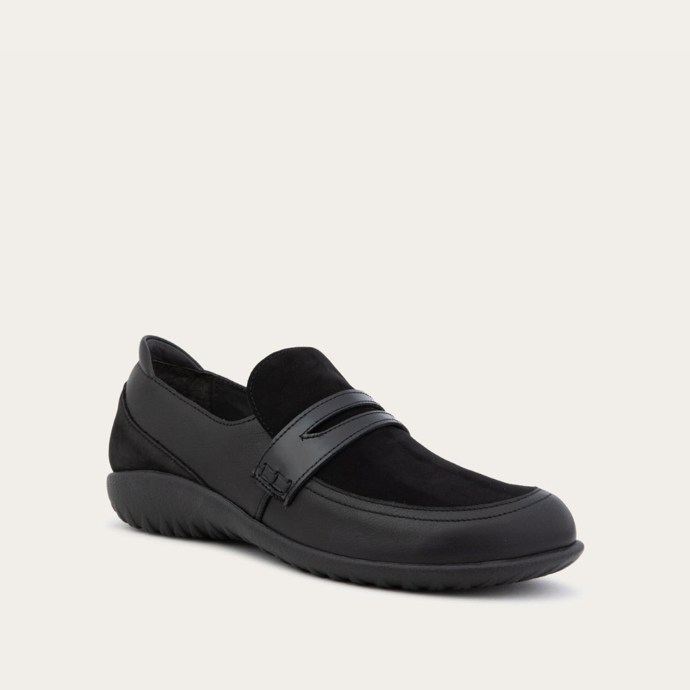 Angled view of a black slip-on loafer featuring a mix of matte leather and soft suede textures with a glossy patent leather strap across the vamp.