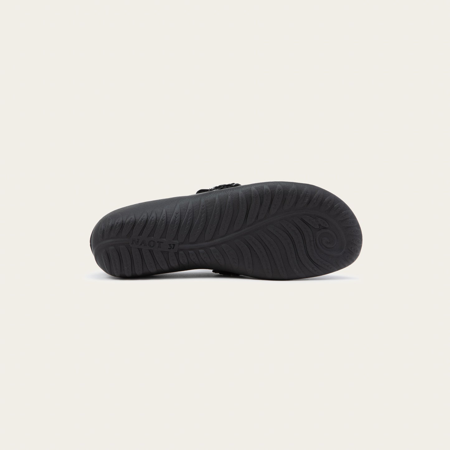 Bottom view of a black slip-on loafer featuring a mix of matte leather and soft suede textures with a glossy patent leather strap across the vamp.