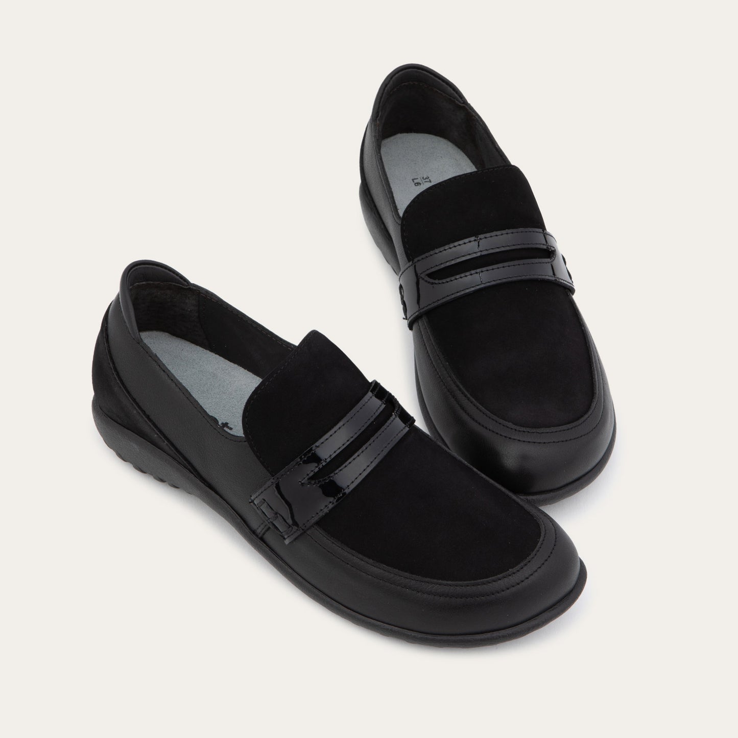 Pair of black slip-on loafers featuring a mix of matte leather and soft suede textures with a glossy patent leather straps across the vamp.