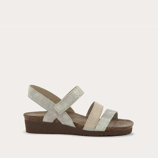 Profile view of a beige sandal with two textured straps and a studded strap on a cork and black rubber sole,