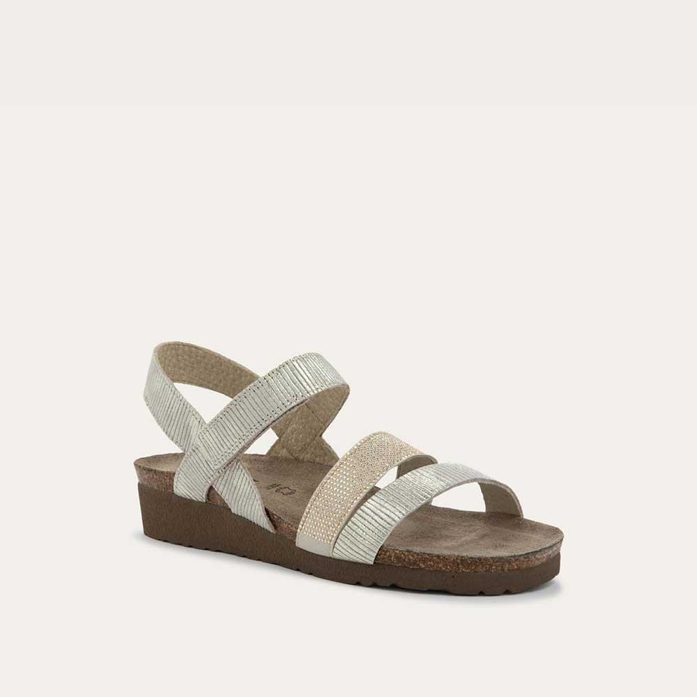 Angled profile view of a beige sandal with two textured straps and a studded strap on a cork and black rubber sole,