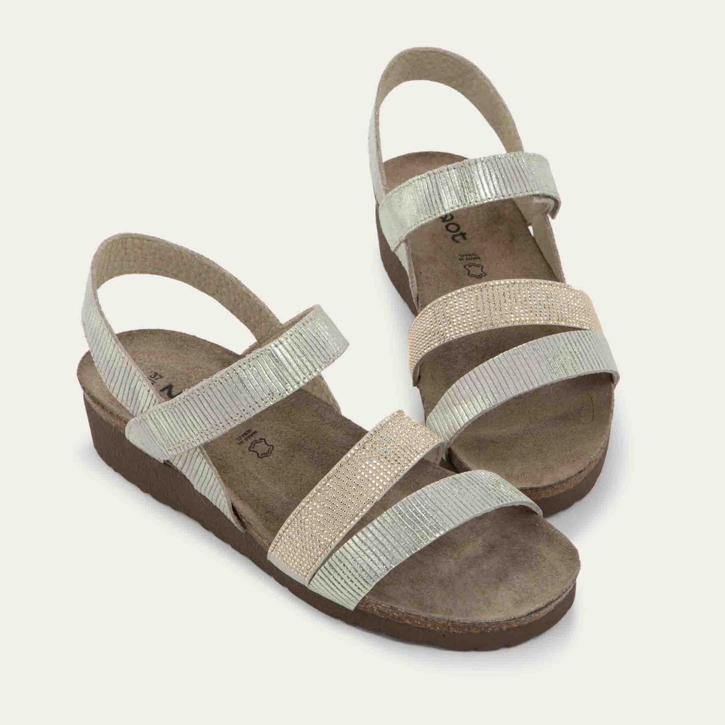 A pair of  beige sandals with two textured straps and a studded strap on a cork and black rubber sole,