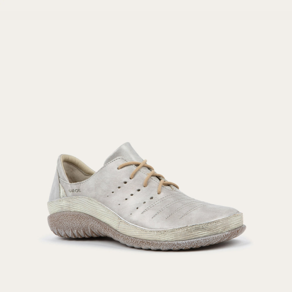 Angled profile view of a casual beige lace-up shoe with textured sole, side perforations, and subtle stitching on a white background, conveying a relaxed, comfortable style.
