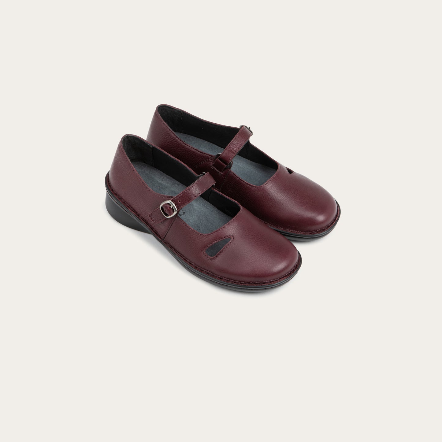 Pair of  red maryjanes on a black sole featuring a simple buckle and small cutout detail on the side