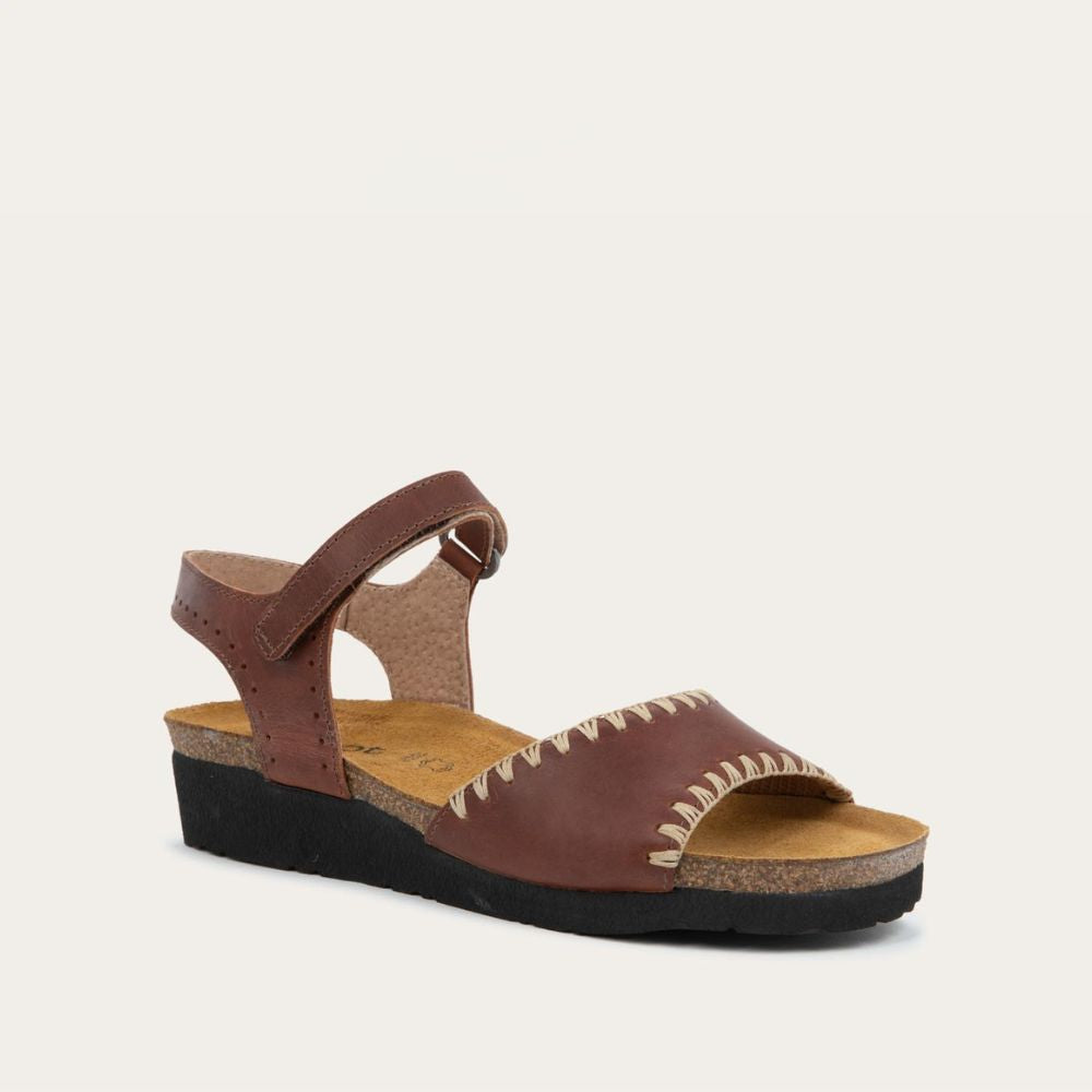 Angled profile view of a brown sandal featuring a toe strap with contrast stitiching, adjustable ankle strap, and a cork footbed.