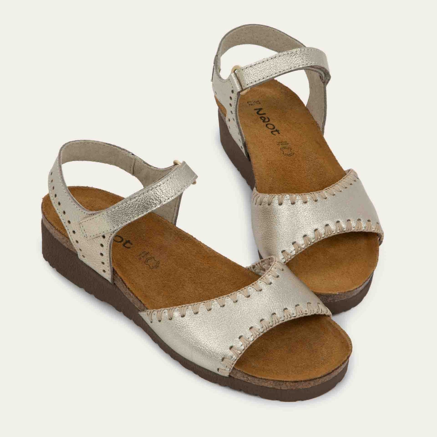 Pair of gold sandals featuring a toe strap with contrast stitiching, adjustable ankle strap, and a cork footbed.