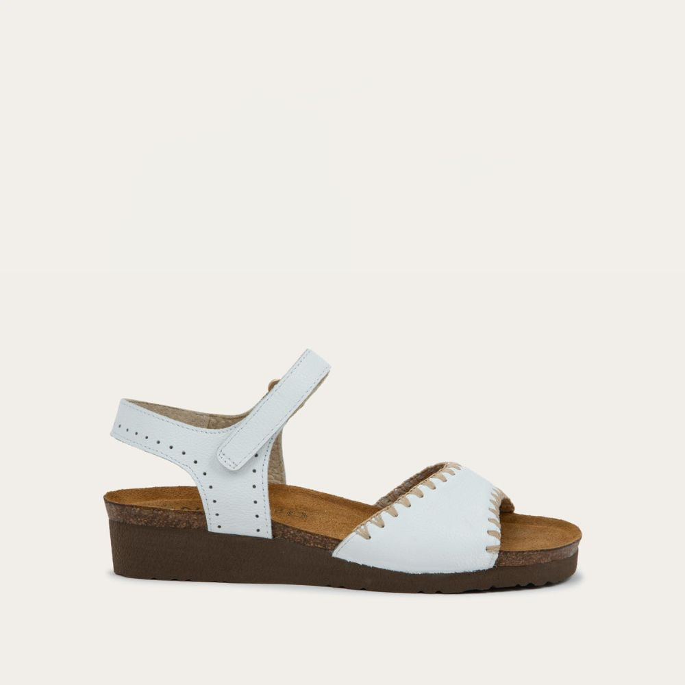 Profile view of  a white sandal featuring a toe strap with contrast stitiching, adjustable ankle strap, and a cork footbed.