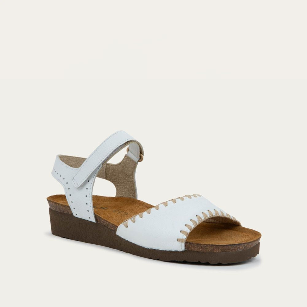 Angled profile view of a white sandal featuring a toe strap with contrast stitiching, adjustable ankle strap, and a cork footbed.