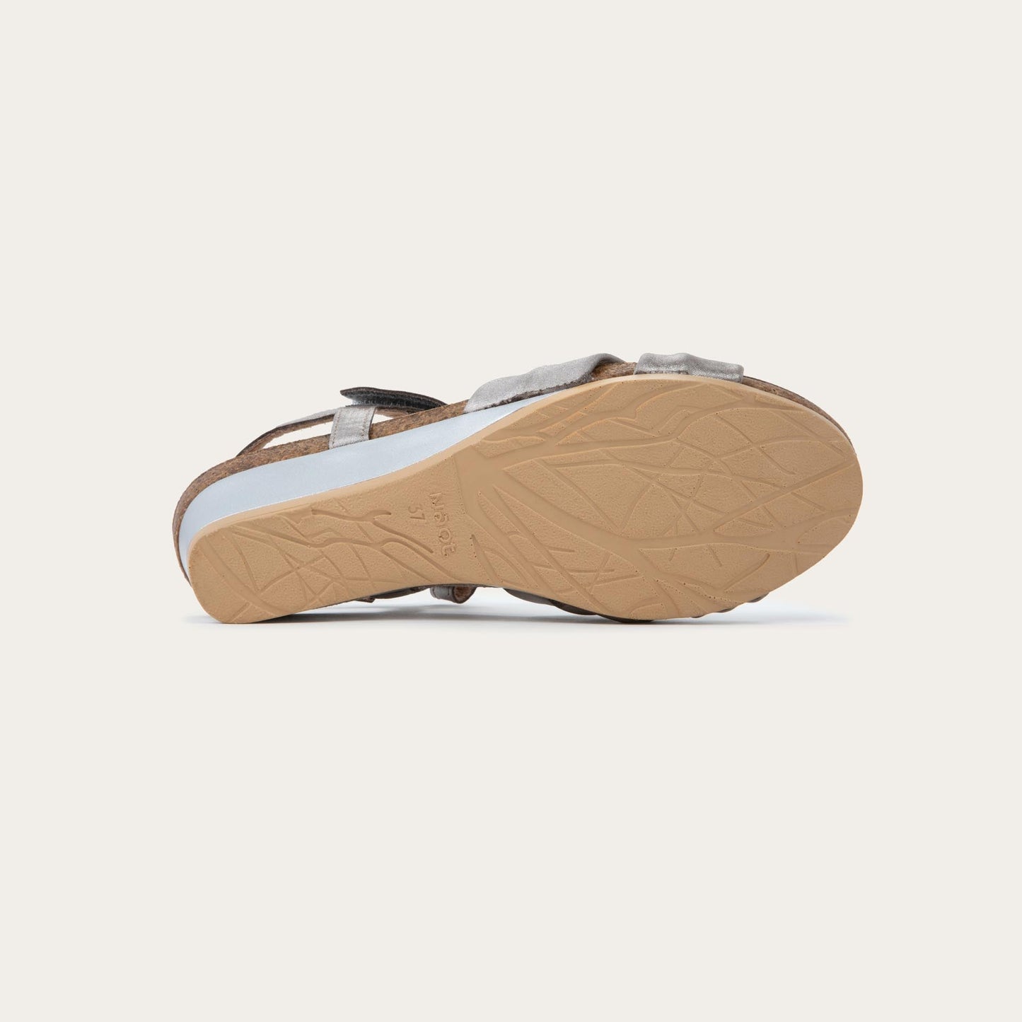 Bottom view of a silver wedge sandal with an ankle strap and twisted front strap, featuring a cork footbed and wedge heel. 