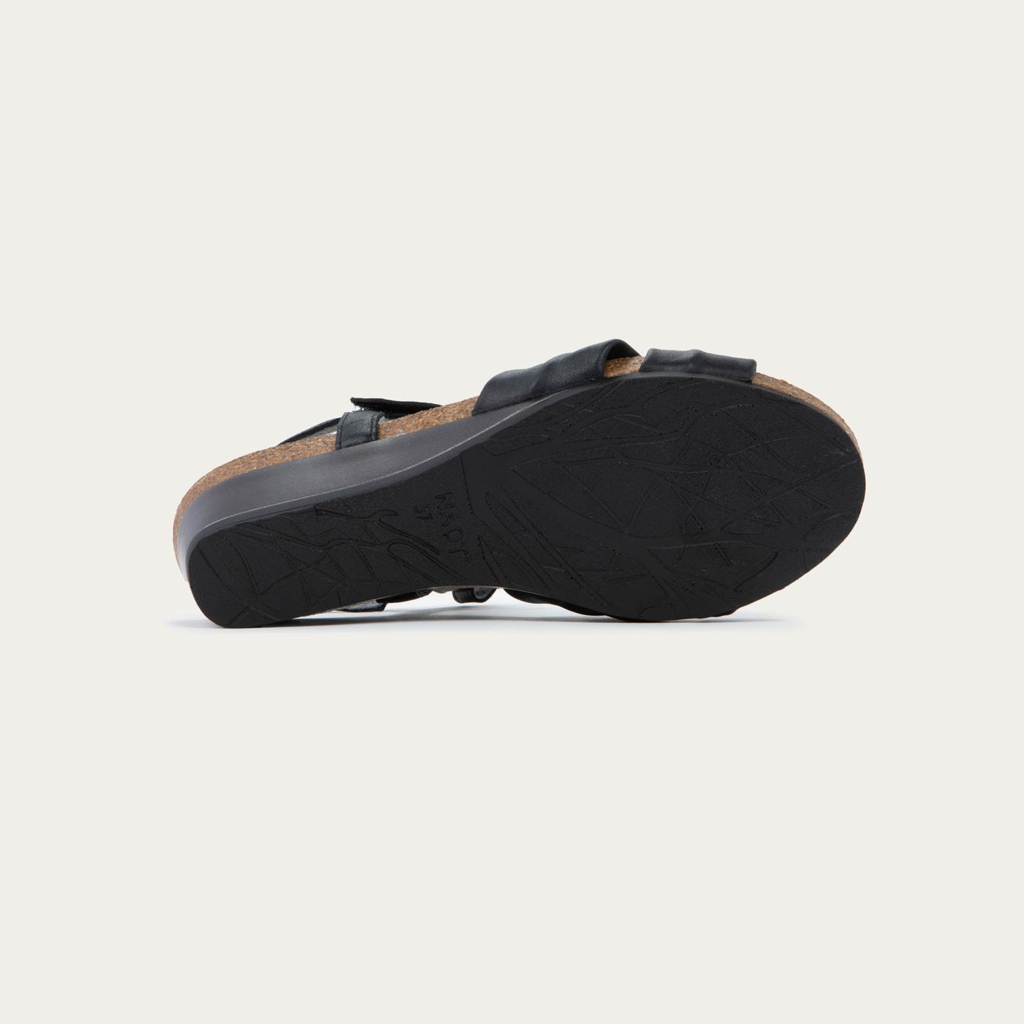 Bottom view of a black wedge sandal with an ankle strap and twisted front strap, featuring a cork footbed and wedge heel. 