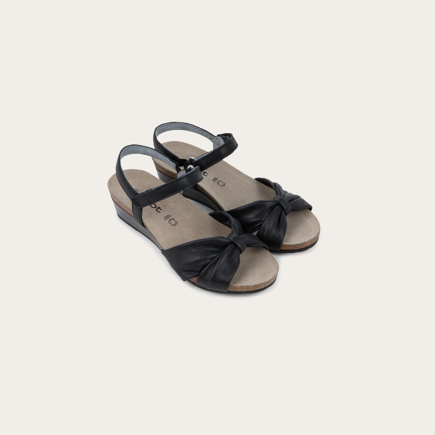 A pair of  black wedge sandals with an ankle strap and twisted front strap, featuring a cork footbed and wedge heel. 