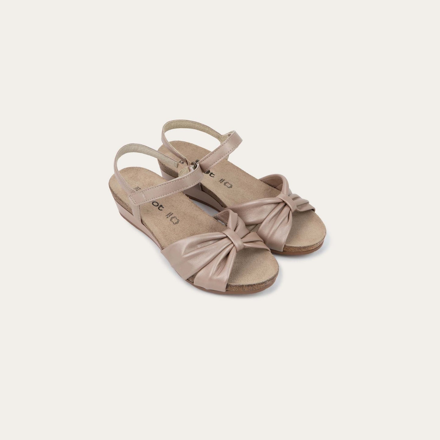 A pair of  mauve wedge sandals with an ankle strap and twisted front strap, featuring a cork footbed and wedge heel. 