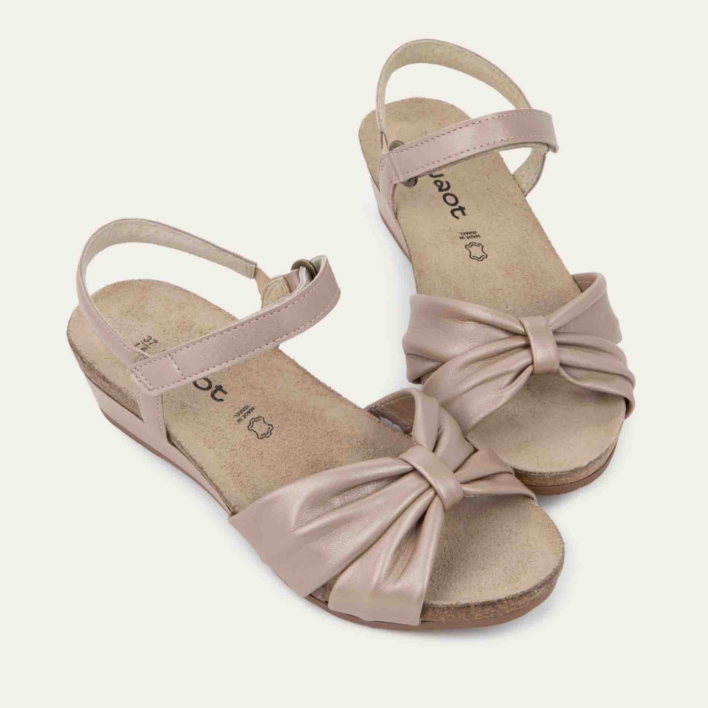A pair of  mauve wedge sandals with an ankle strap and twisted front strap, featuring a cork footbed and wedge heel. 