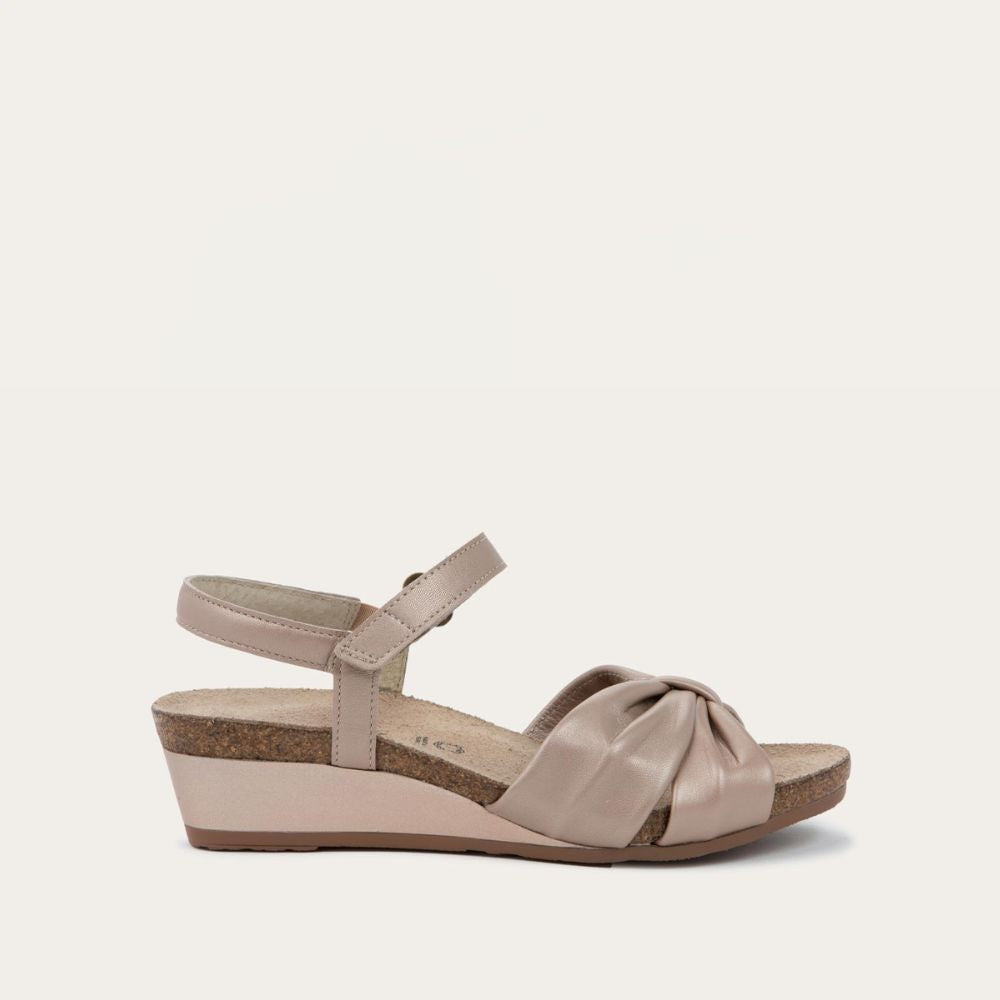 Profile view of a mauve wedge sandal with an ankle strap and twisted front strap, featuring a cork footbed and wedge heel. 