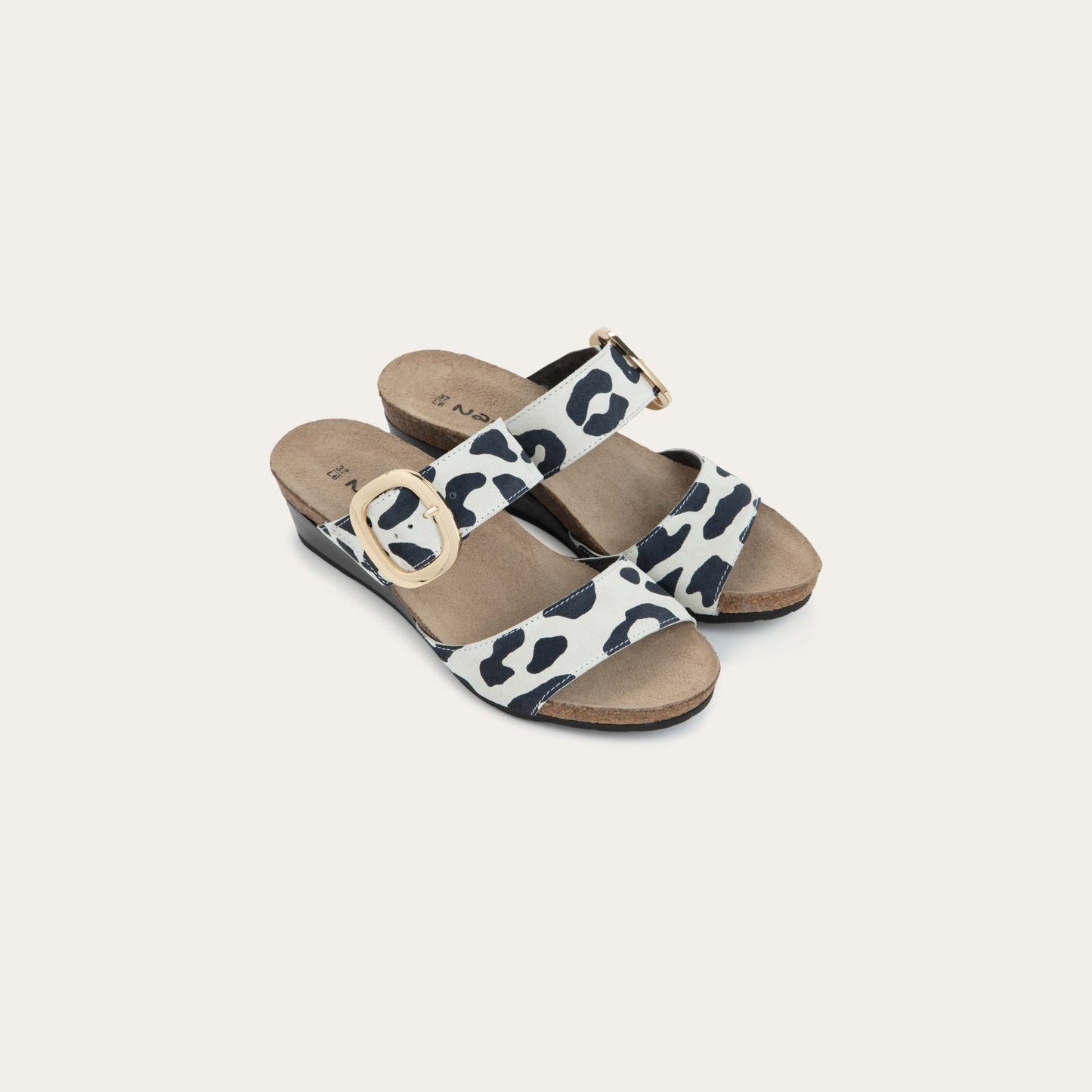 Pair of black and white leaopard-print slip on wedge sandals with two straps and a large gold buckle. 
