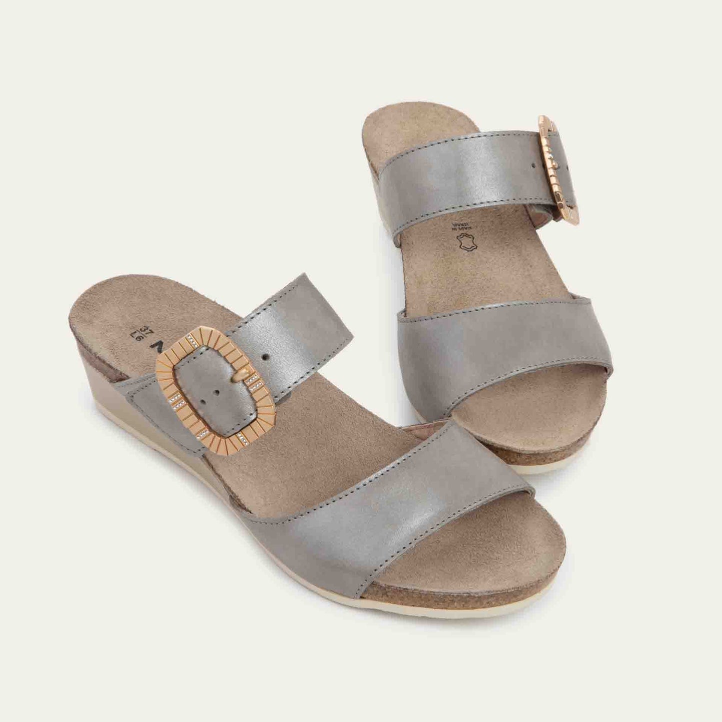 Pair of metalic gray slip-on wedge sandals with two straps and a large textured buckle. 